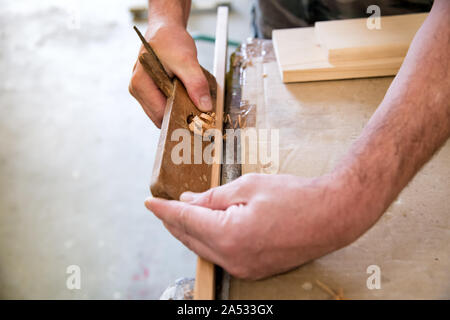 Tischler mit einem Planer auf ein Brett aus Holz in einem Holzbearbeitung Workshop in einer Nahaufnahme auf seine Hände, die Holzteile auf der Werkbank Stockfoto