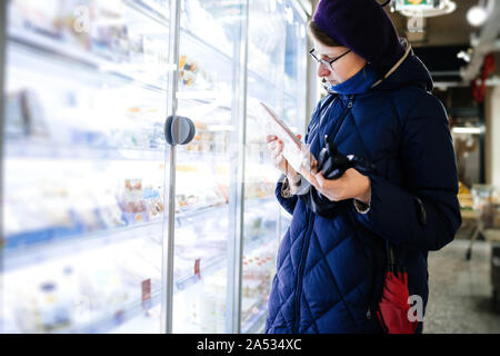 Neugierig Frau liest Zusammensetzung eines Erzeugnisses aus dem Kühlschrank in Bio Supermarkt Stockfoto