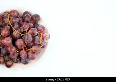 Rote Trauben auf einem Rosa auf weißem Hintergrund. Ansicht von oben Stockfoto