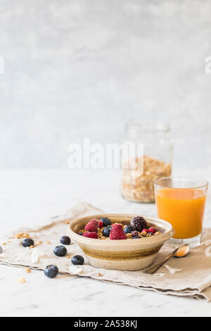 Ein frisches und gesundes Frühstück mit Müsli Müsli, frischen Beeren - Heidelbeeren, Himbeeren. Orangensaft, Müsli und ein jar im Hintergrund. Vertikale Stockfoto