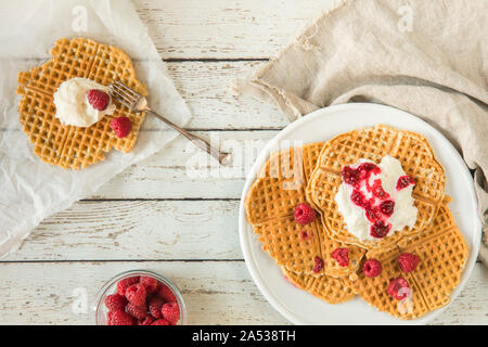 Waffeln mit Himbeeren und Sahne von oben, flach legen Vorausschau - gesehen. Es ist eine Glasschale mit ganzen Himbeeren auf dem Tisch, eine Gabel und einer Linie Stockfoto