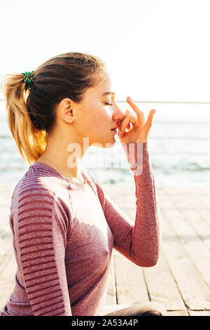Junge Frau, Pranayama, der am Ufer des Meeres in der Morgendämmerung Stockfoto