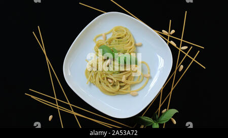 Konzept der italienisches Essen. Teller Pasta Spaghetti mit Pesto. Schwarzer Hintergrund mit Spaghetti, Basilikum und Pinienkernen. Ansicht von oben, von oben. Stockfoto