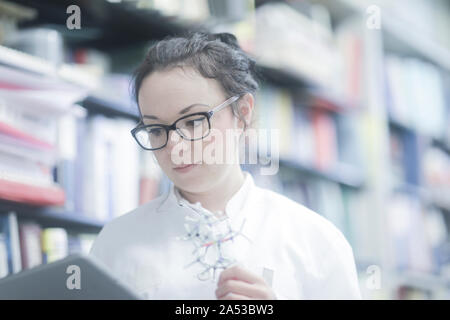 Junge Wissenschaftler mit Tablette in einer Bibliothek mit einem Modell Stockfoto