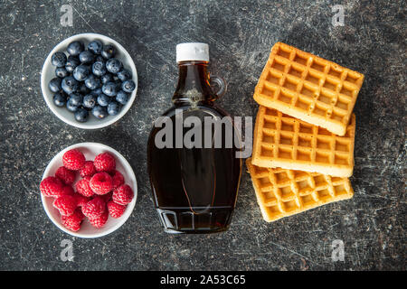 Waffeln, Ahornsirup, Heidelbeeren und Himbeeren auf alten Küche Tisch. Ansicht von oben. Flache Ansicht. Stockfoto