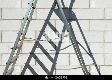 Close-up mittlere Teil der alten verwendete Metall zerlegbare Skalierung Leiter an der Wand von Porenbeton Hintergrund in hellem Sonnenlicht. Stockfoto