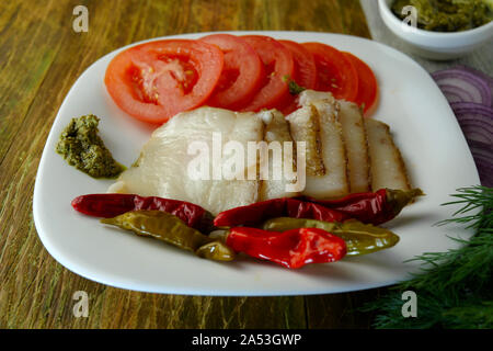 Appetitliche Snacks. In Scheiben geschnitten ​​Smoked Schweineschmalz, Tomaten, eingelegte Paprika und Pesto liegen auf braunem Holz- Oberfläche. Close-up. Stockfoto