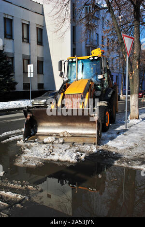 Leuchtend gelben Bagger Traktor Reinigung Schnee auf der Straße entlang der Häuser, Vorderansicht, schneereichen Winter in Charkow, Ukraine Stockfoto