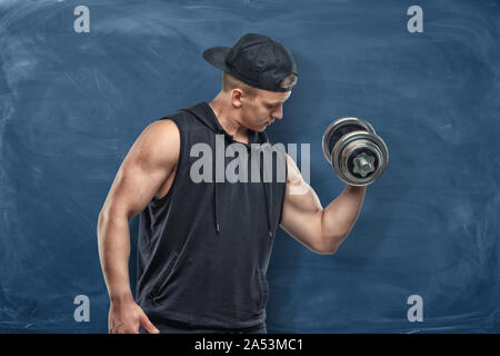 Porträt der jungen gutaussehenden Mann im schwarzen Outfit stehen und zeigt seine Muskeln Bizeps während des Trainings Stockfoto