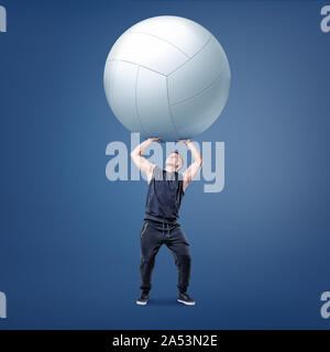 Eine kleine muskulöse Athleten hält einen großen weißen volleyball Ball auf Gerade arme über sich. Stockfoto