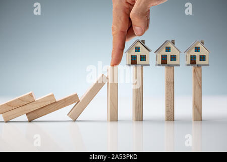 Nahaufnahme der Holzblock inmitten Modell Haus und Dominosteine, die Versicherung auf Tisch Stockfoto