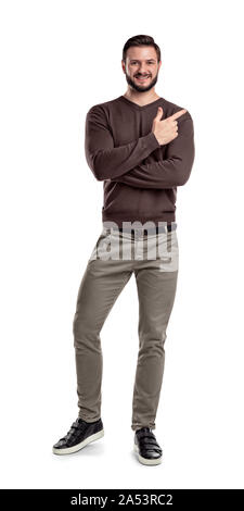 Ein bärtiger Mann in legere Kleidung hält ein Bein gebogen Weiß lächelnd und zeigt Richtung mit einem gekreuzten Händen. Stockfoto