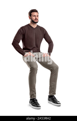 Eine isolierte bärtigen Mann in Freizeitkleidung sitzt auf einem weißen Hintergrund mit den Händen auf seinen Oberschenkeln. Stockfoto