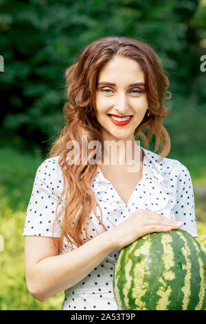 Hübsche Frau hält eine ganze Wassermelone im Freien. Schöne Mädchen hält eine ganze Wassermelone in der Natur. Stockfoto