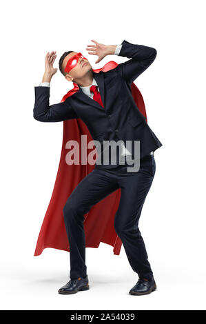 Ein Geschäftsmann in einem Helden rotem Umhang und eine Maske, in der Ansicht von vorn geduckt in Angst auf weißem Hintergrund. Stockfoto