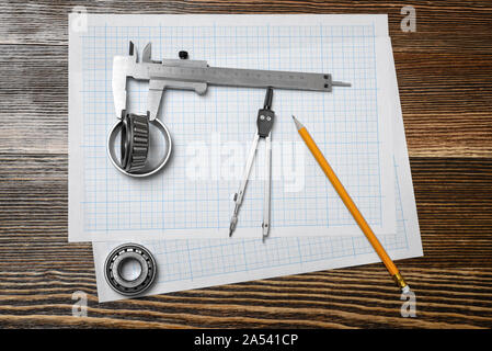 Ein messschieber Holding ein Lager, einen Bleistift und einen Zirkel über Ausarbeitung Papier auf Holz Hintergrund liegt. Stockfoto