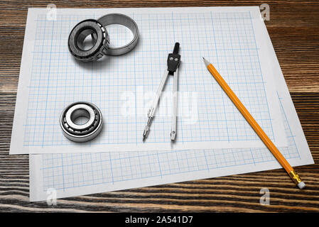 Ein messschieber Holding ein Lager, einen Bleistift und einen Zirkel über Ausarbeitung Papier auf Holz Hintergrund liegt. Stockfoto