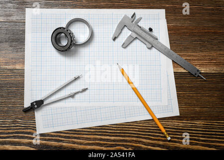 Ein messschieber Holding ein Lager, einen Bleistift und einen Zirkel über Ausarbeitung Papier auf Holz Hintergrund liegt. Stockfoto