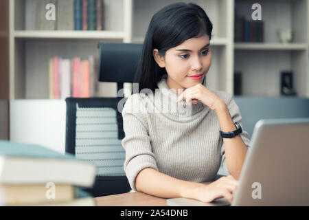 Asiatische junge intelligente Frau Manager mit casual Ihr Geschäft arbeiten mit Laptop und sitzen auf Stuhl Gefühl im legeren Outfit überzeugt. Headshot von f Stockfoto