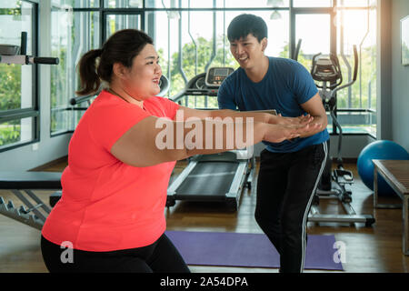 Zwei asiatische Trainer Mann und übergewichtige Frau zusammen Training zu dehnen im modernen Fitnessraum, glücklich und Lächeln während des Trainings. Dicke Frauen kümmern sich um Gesundheit. Stockfoto