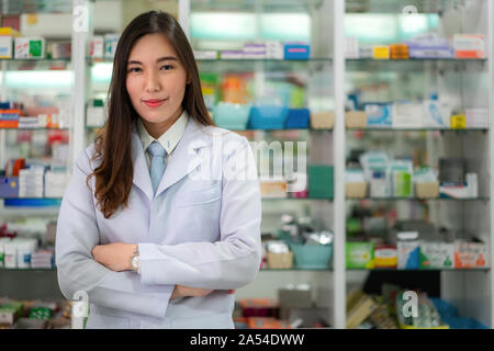 Zuversichtlich asiatische Junge weibliche Apotheker mit einem reizenden Lächeln stand mit verschränkten Armen in der Apotheke und Drogerie. Medizin, Pharmazie, hea Stockfoto