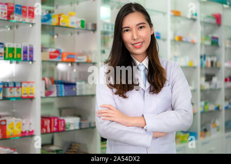 Zuversichtlich asiatische Junge weibliche Apotheker mit einem reizenden Lächeln stand mit verschränkten Armen in der Apotheke und Drogerie. Medizin, Pharmazie, hea Stockfoto