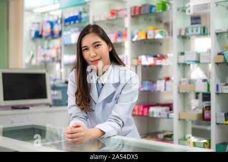 Zuversichtlich asiatische Junge weibliche Apotheker mit einem reizenden Lächeln gestützt auf einem Schreibtisch in der Apotheke und Drogerie. Medizin, Pharmazie, er Stockfoto