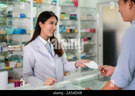 Zuversichtlich asiatische Junge weibliche Apotheker mit einem freundlichen Lächeln empfangen und Medizin Rezept von man Patienten in der Apotheke und Drogerie. Med Stockfoto