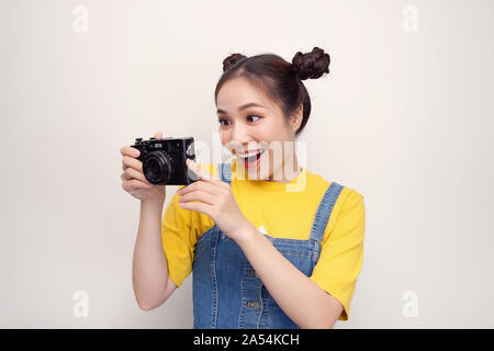 Überrascht, Frau, mit top knot Frisur, das Tragen von Jeans Overall, Holding retro Kamera, auf dem weißen Hintergrund Stockfoto