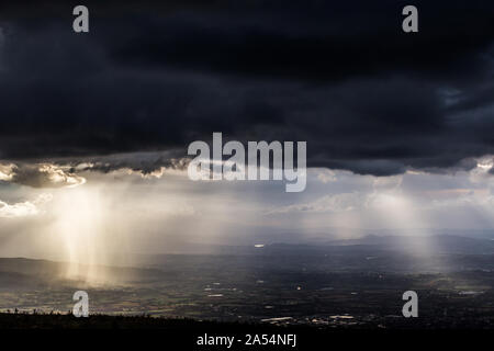 Sonnenstrahl scheint durch Wolken und Regen über die Berge in der Mitte der Schatten Stockfoto