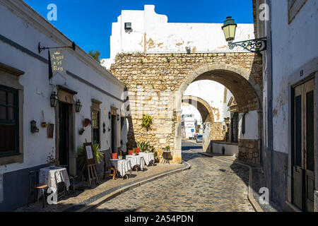 Malerischen gepflasterten Straße in Faro Altstadt vorbei unter Arco do Repouso. Faro, Algare, Portugal, April 2019 Stockfoto