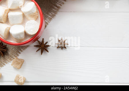 Rot Tasse heiße Schokolade mit Zucker und Anis Gewürze auf sackleinen und weiße Holztisch Hintergrund. Platz für Text. Weihnachten Hintergrund. Stockfoto