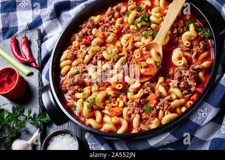 In der Nähe von amerikanischen italienischen Gulasch Ellenbogen Makkaroni, Rindfleisch, Sellerie und Tomaten in einer schwarzen Keramik Teller auf einen Holztisch mit Küchentuch, Aussicht f Stockfoto