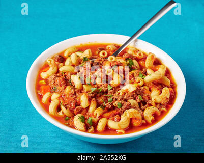 Portion Gulasch Ellenbogen Nudeln, Rindfleisch, Sellerie und Tomaten in einer weißen Schüssel mit dem Löffel serviert, Ansicht von oben, close-up Stockfoto