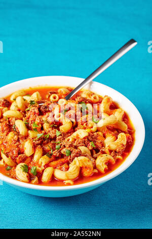 Portion Gulasch Ellenbogen Nudeln, Rindfleisch, Sellerie und Tomaten in einer weißen Schüssel serviert auf einem blauen textile Matte, Ansicht von oben, close-up Stockfoto