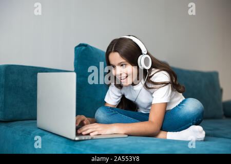 Cute Teenager Mädchen in Kopfhörer auf dem Sofa mit Laptop Musik hören Stockfoto