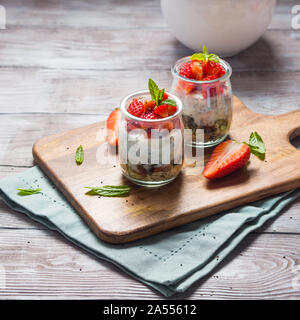 Joghurt Müsli Parfait mit Erdbeeren und Chia Samen. Gesunde Single-portion-Frühstück serviert im Glas Tassen auf Holzbrett mit grünen Serviette. Natu Stockfoto