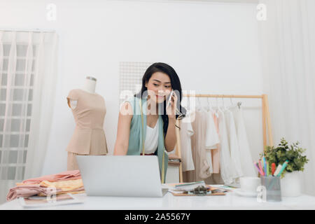 Junge asiatische Fashion Designer/business mit Laptop und Aufruf an Ihr Studio Stockfoto