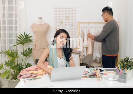 Fashion Designer bei der Arbeit. Stattliche männliche Designer Wahl entwerfen, während sein Kollege arbeiten mit Laptop. Stockfoto