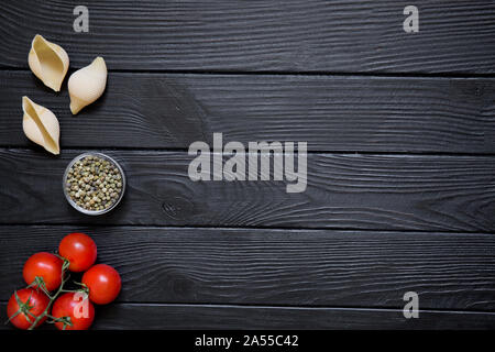 Zutat für die Italienische Küche Gerichte auf schwarzen Holztisch Hintergrund. Big conchiglie, rote Kirschen, Tomaten und Paprika. Kopieren Sie Platz. Stockfoto