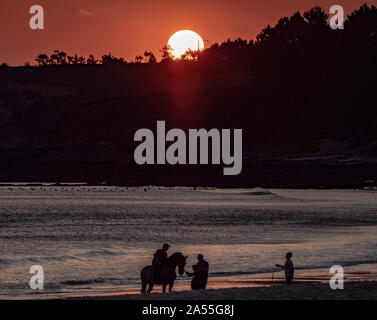 Schuss auf eine Gruppe von Menschen die Silhouetten am Strand reiten und Spritzwasser einige Wellen entlang der Küste Stockfoto