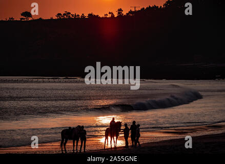 Schuss auf eine Gruppe von Menschen die Silhouetten am Strand reiten und Spritzwasser einige Wellen entlang der Küste Stockfoto