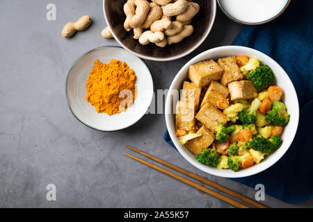 Rühren gebratener Tofu und Gemüse mit Satay Sauce in einer Schüssel auf einem Stein. Ansicht von oben Stockfoto