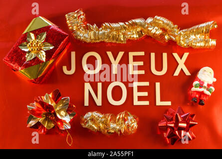 Frohe Weihnachten in französischer Sprache mit Geschenk und Weihnachtsschmuck auf rotem Hintergrund geschrieben Stockfoto