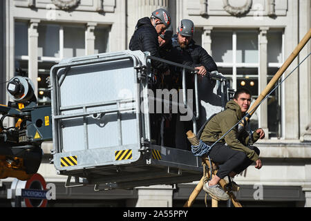 Polizei versucht eine Demonstrantin, die saß auf einem Bambus Struktur der Straße am Oxford Circus, London, während einer Aussterben Rebellion (XR) Klimawandel protest Block ist zu entfernen. Stockfoto