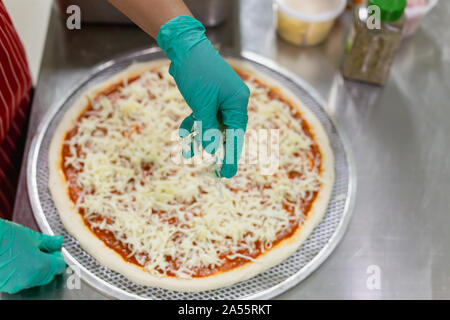 Cook's Hand mit grünen Handschuhen, Käse auf der Pizza. Stockfoto