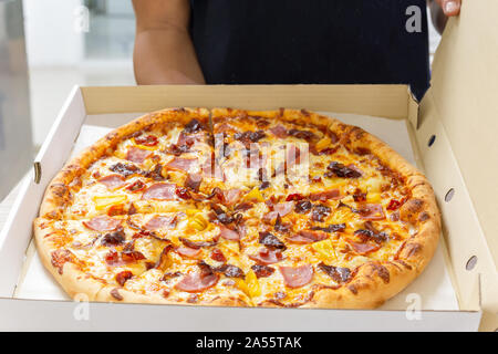 Mann hält ein Open Box von Pizza in der Hand und bietet es für andere. Stockfoto