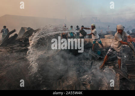 Navotas City, Philippinen. Okt, 2019 18. Menschen gießen Sie Wasser auf eine verbleibende Feuer wie andere Bewohner für ihre Habseligkeiten durch ihre Verkohlten Wohnungen suchen Sie nach einem Brand in einem Wohngebiet im Navotas City, Philippinen, Okt. 18, 2019. Nach den Navotas Stadt Katastrophenvorsorge Management Office, rund 200 Baracken waren im Feuer zerstört. Credit: rouelle Umali/Xinhua/Alamy leben Nachrichten Stockfoto