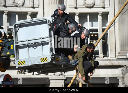 Polizei versucht eine Demonstrantin, die saß auf einem Bambus Struktur der Straße am Oxford Circus, London, während einer Aussterben Rebellion (XR) Klimawandel protest Block ist zu entfernen. Stockfoto