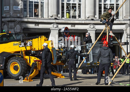 Polizei versucht eine Demonstrantin, die saß auf einem Bambus Struktur der Straße am Oxford Circus, London, während einer Aussterben Rebellion (XR) Klimawandel protest Block ist zu entfernen. Stockfoto